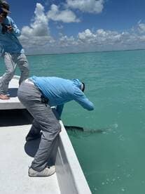 Two anglers actively fishing from a boat, with one preparing to reel in a fish in the clear waters of a tropical fishing environment.