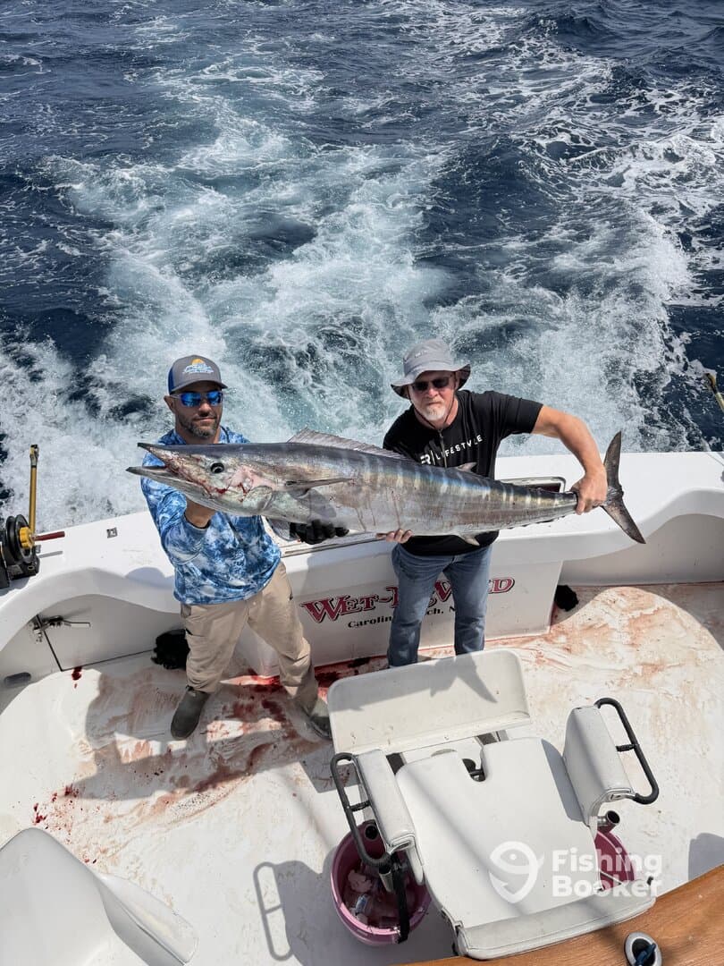 Two anglers proudly displaying a large Wahoo on a sportfishing boat, showcasing a successful deep-sea fishing trip.
