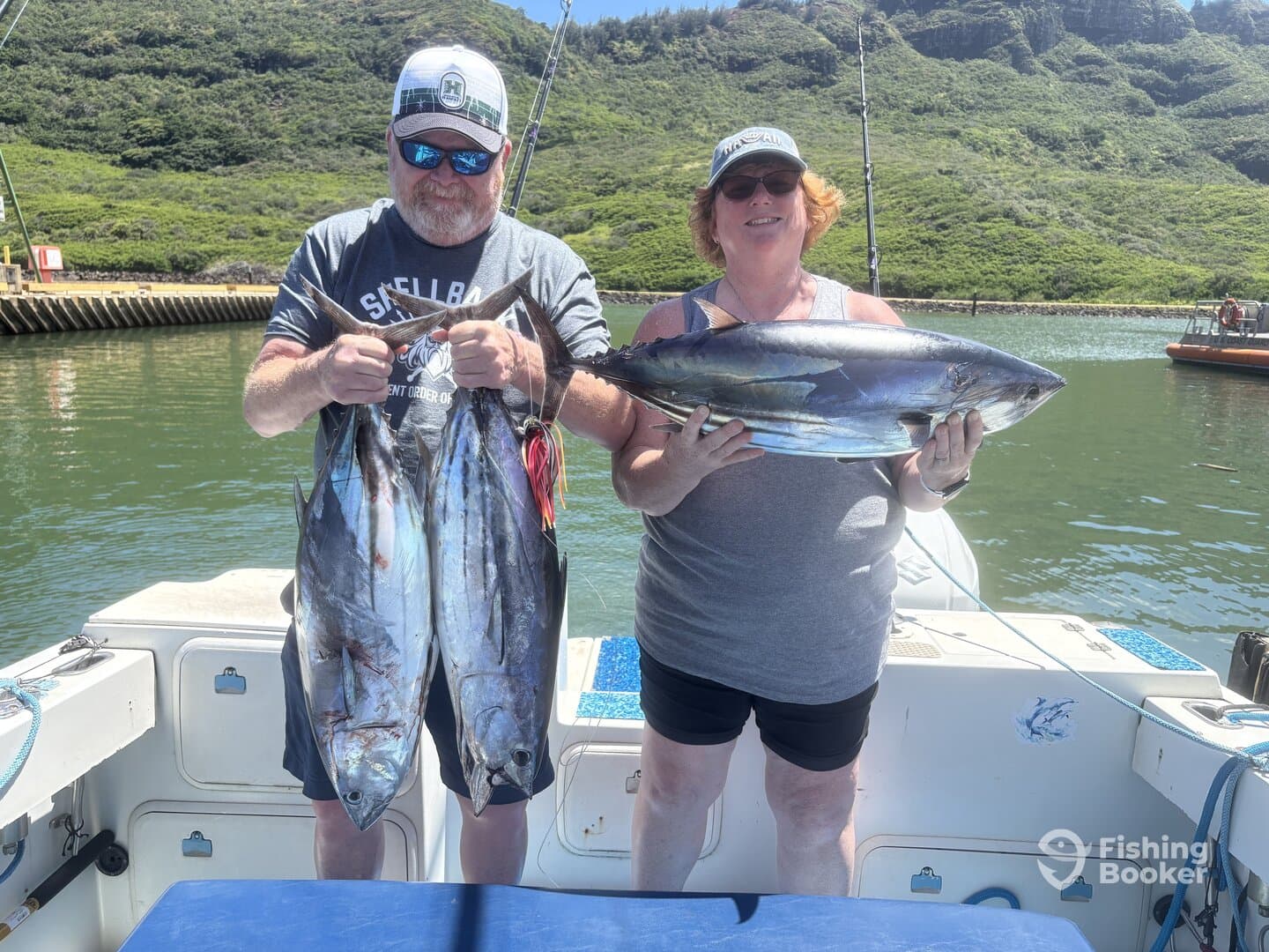 Two anglers proudly displaying their catch of Tuna while on a fishing charter in a scenic coastal environment.