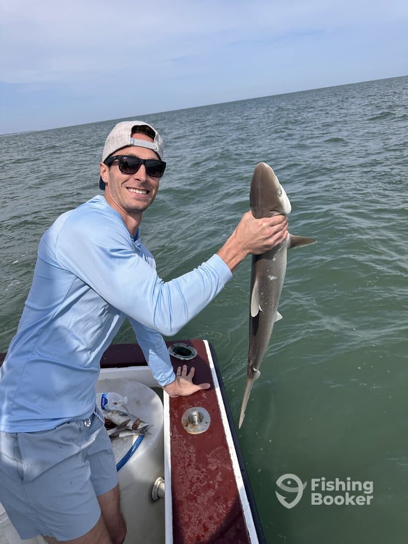 Angler proudly displaying a caught shark while fishing from a boat in open waters.