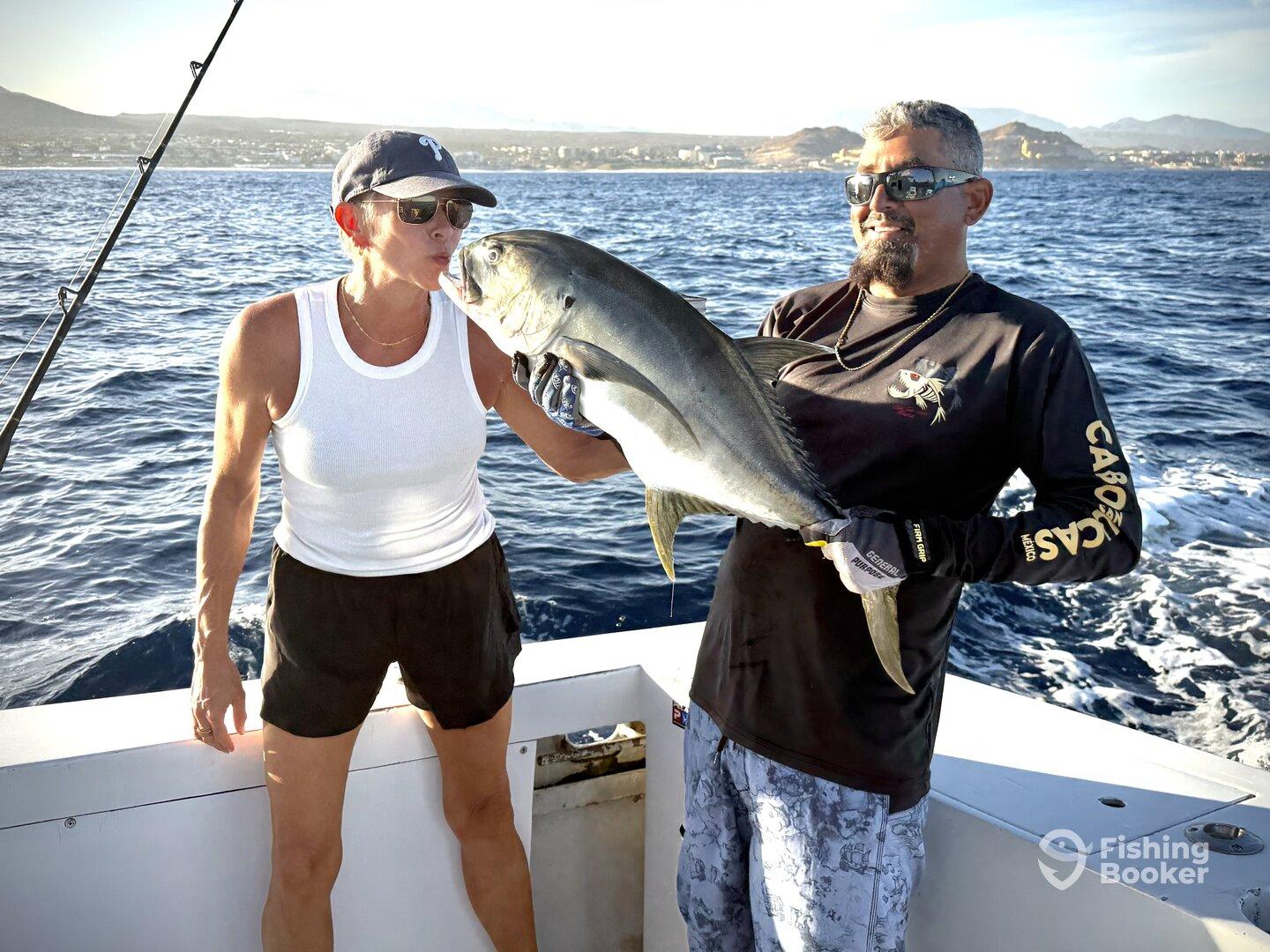 Two anglers proudly displaying a large fish on a boat in the ocean, showcasing a successful fishing trip.