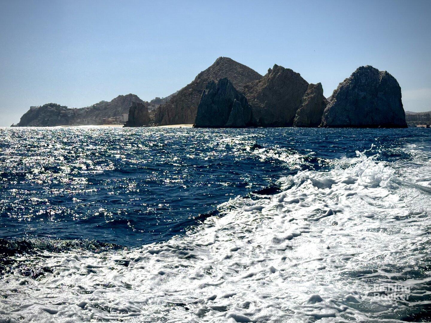 Scenic view of rocky cliffs and sparkling waters, captured from a boat near Cabo San Lucas, showcasing the beautiful coastal landscape.
