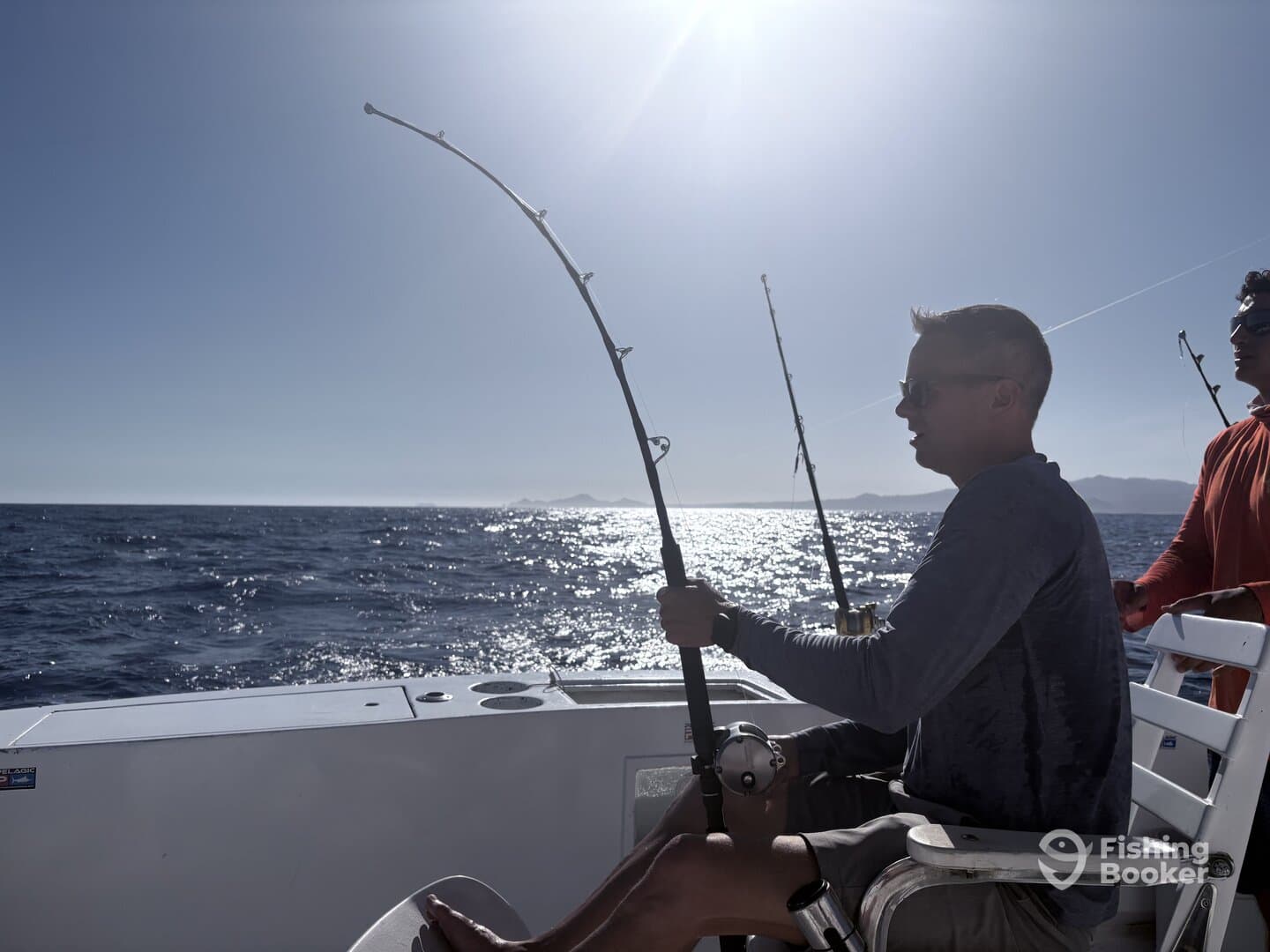 Two anglers actively fishing on a boat, with one reeling in a line while enjoying a sunny day on the water.