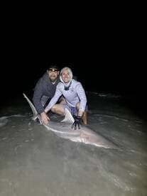Two anglers proudly displaying a large shark caught during a night fishing session on the beach.