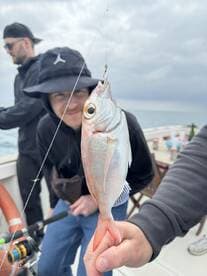 Angler proudly displaying a freshly caught fish while fishing on a boat, showcasing a casual group fishing experience.