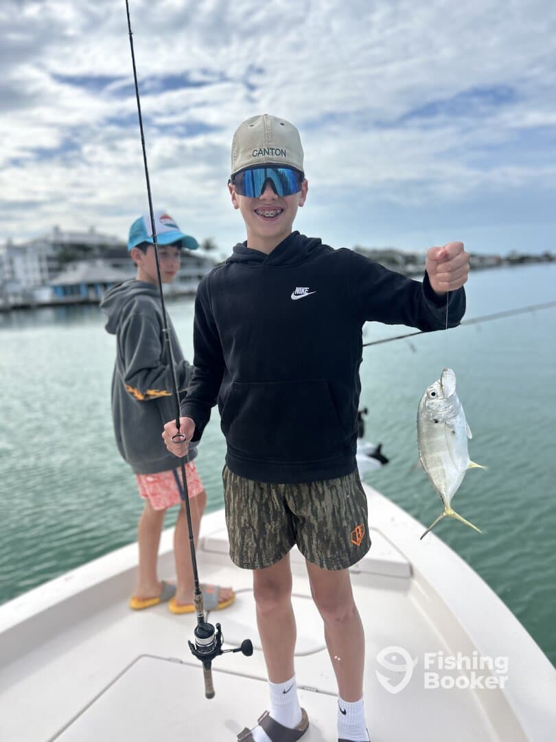 A young angler proudly displaying a small fish while fishing from a boat, with another child in the background, enjoying a day on the water.