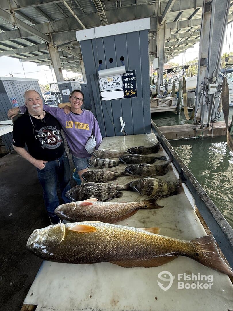 Two anglers proudly displaying a variety of fish, including large Redfish, on a cleaning table at a marina after a successful fishing trip.