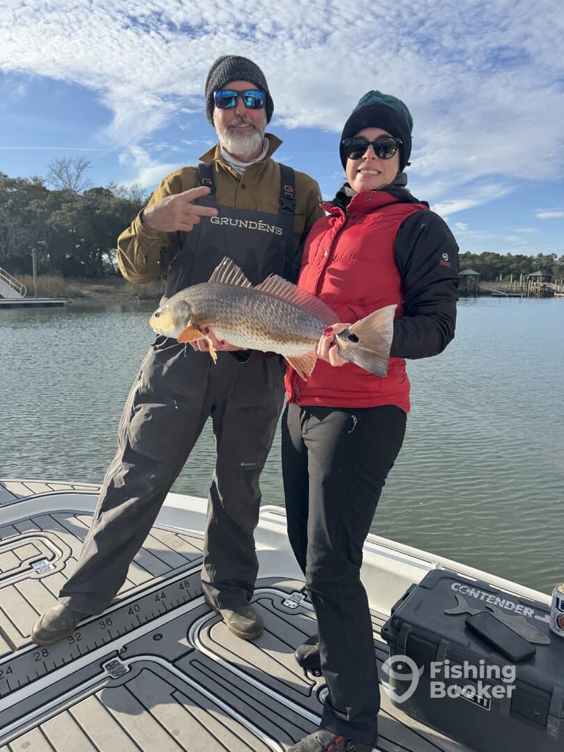 Two anglers proudly displaying a Redfish on a boat, showcasing a successful fishing trip.