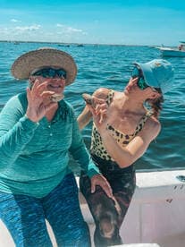 Two women enjoying a day on the water, showcasing their catch of clams while relaxing on a boat.
