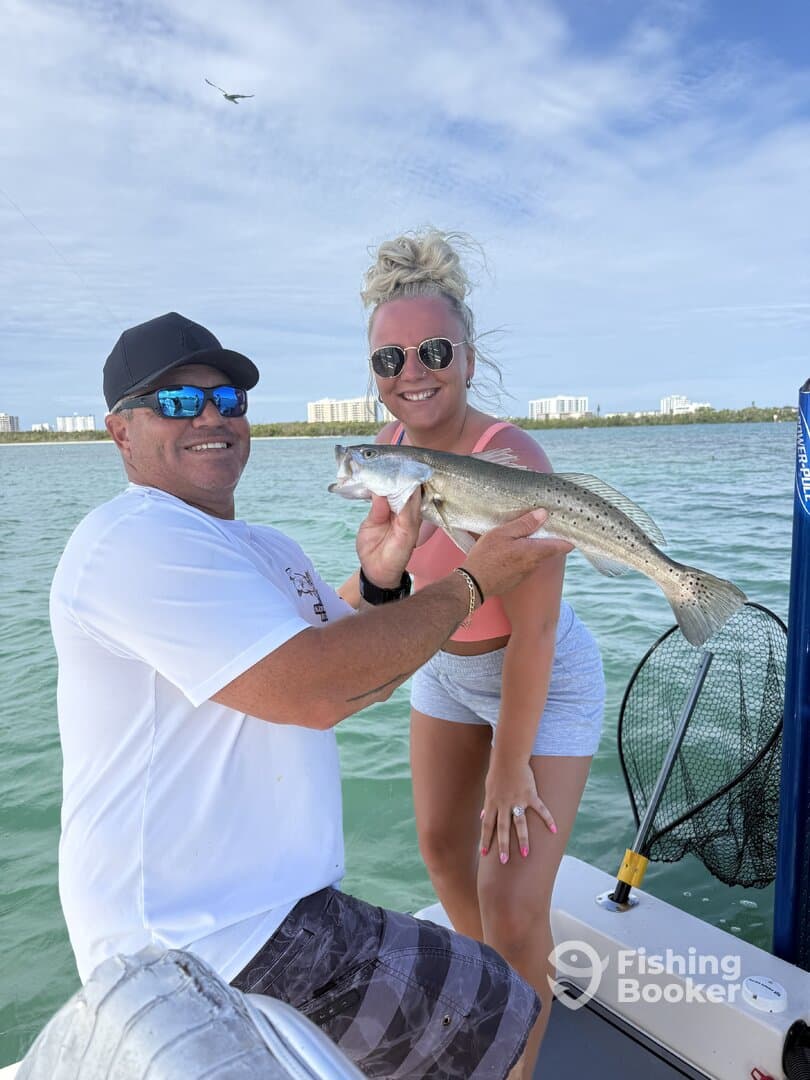 Two anglers proudly displaying a Speckled Trout while fishing in a coastal environment.