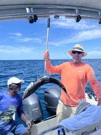 Two anglers celebrating a successful catch of a large fish while out on the open water, showcasing their excitement and teamwork.