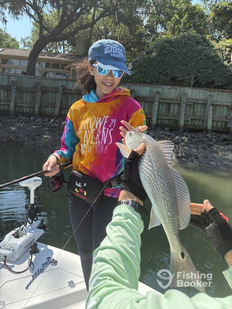 A young angler proudly displaying a freshly caught fish while fishing from a boat in a scenic waterway.