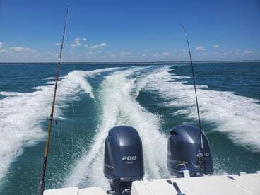 A scenic view from the back of a boat, showcasing twin Yamaha outboard motors and the wake created as the boat moves through the clear blue waters.