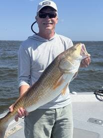Angler proudly displaying a large Redfish while fishing on a sunny day.