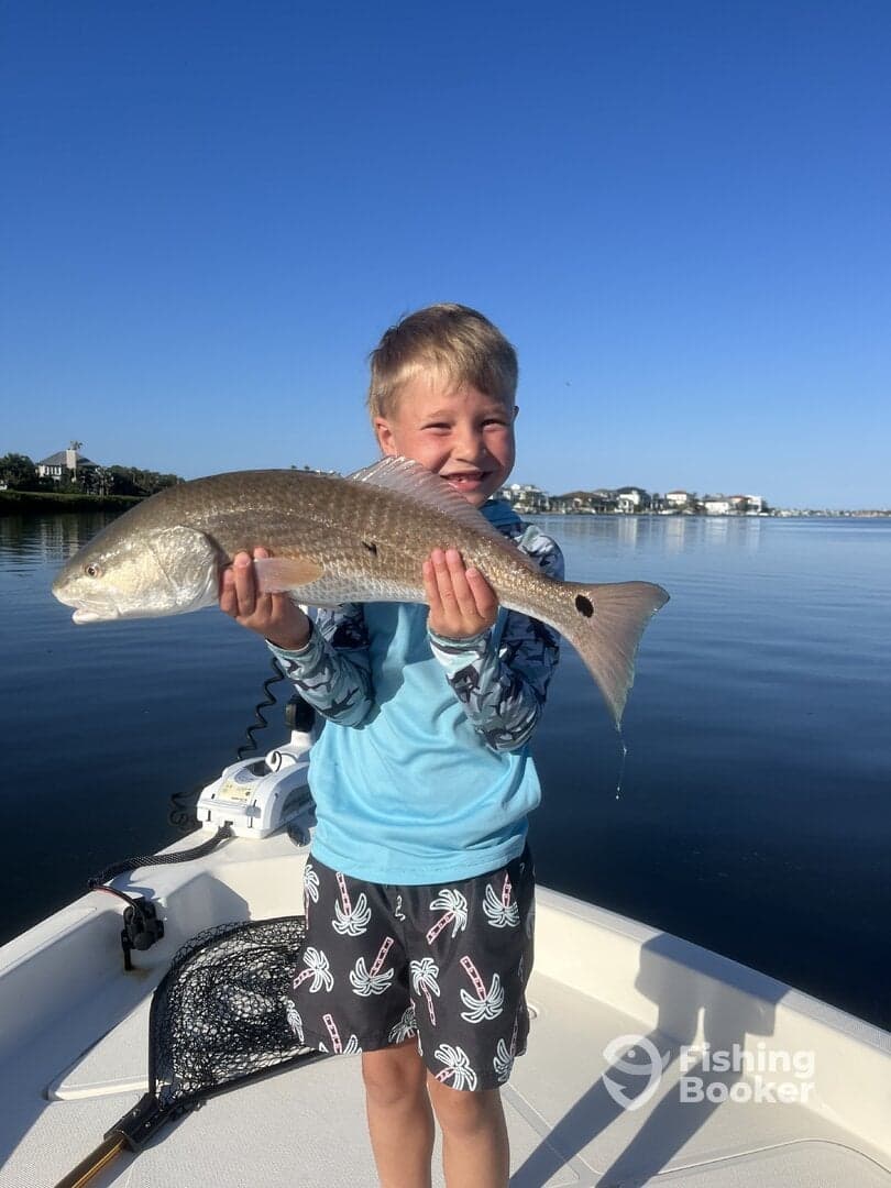 A young angler proudly holding a Redfish while fishing from a boat on a calm day.