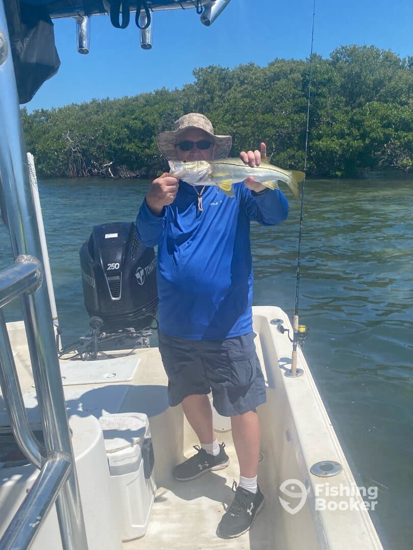Angler proudly displaying a Snook caught while fishing in a mangrove area, showcasing a sunny day on the water.