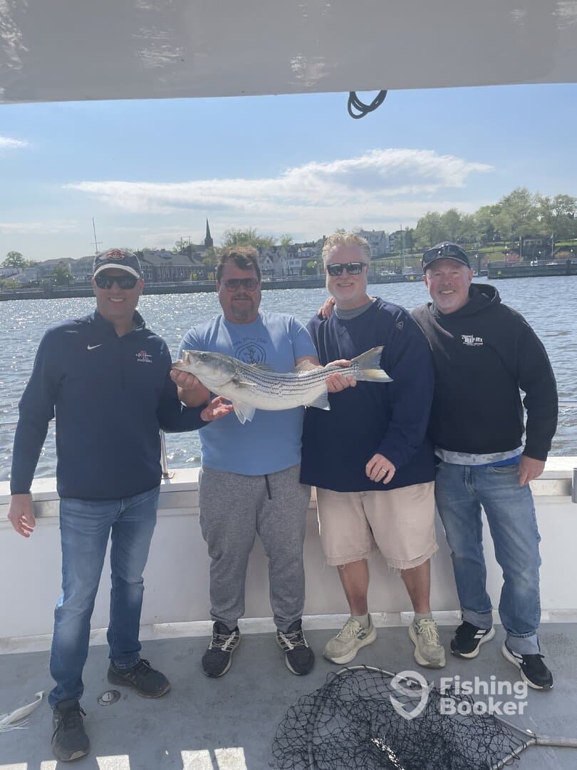 A group of anglers proudly displaying a large Striped Bass on a fishing charter, enjoying a sunny day on the water.