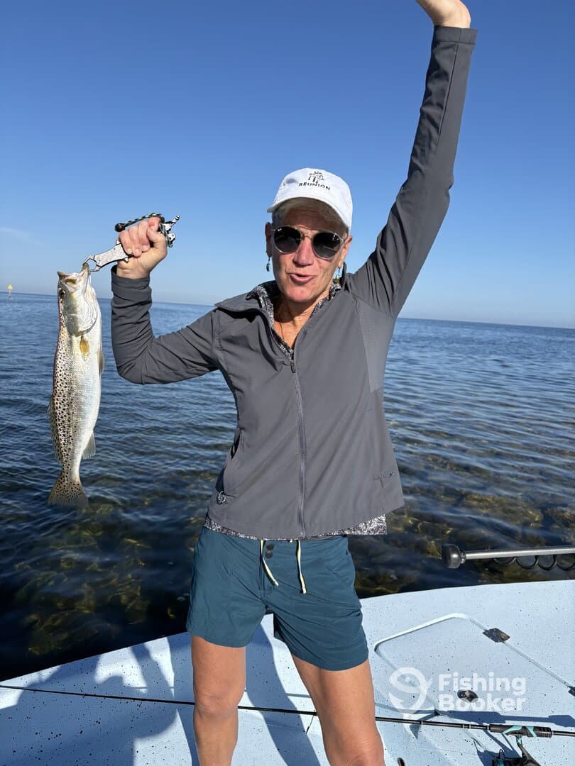 Angler proudly displaying a large Speckled Trout while fishing on a sunny day.