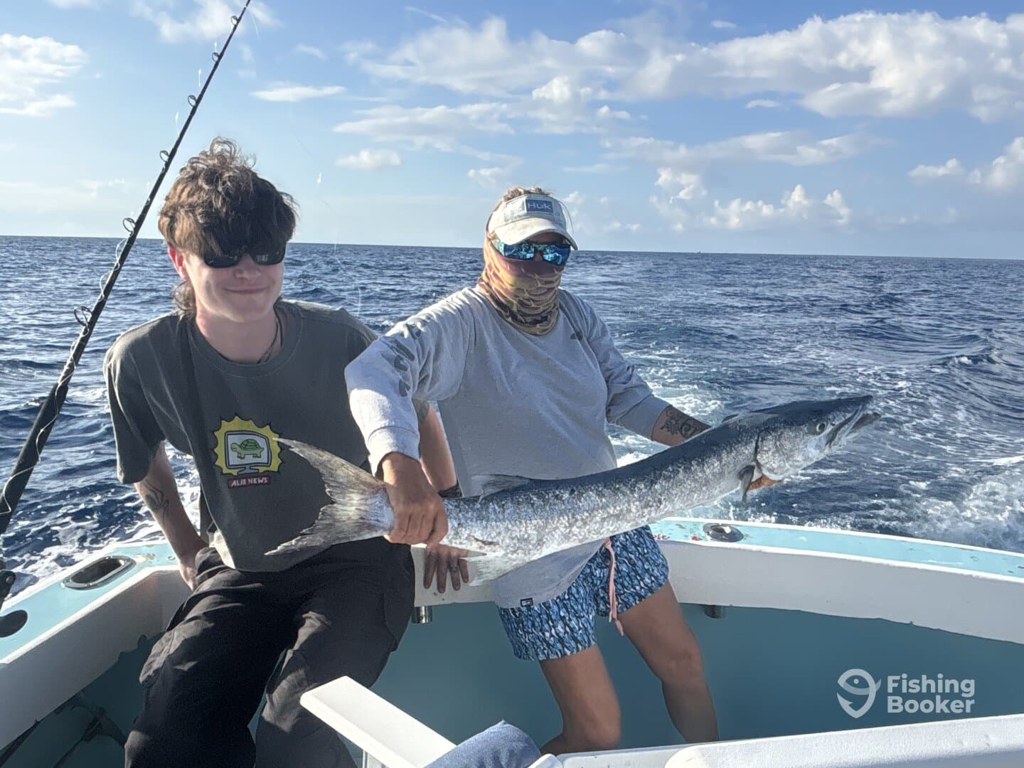 Two anglers proudly displaying a large Barracuda while fishing offshore, enjoying a sunny day on the water.