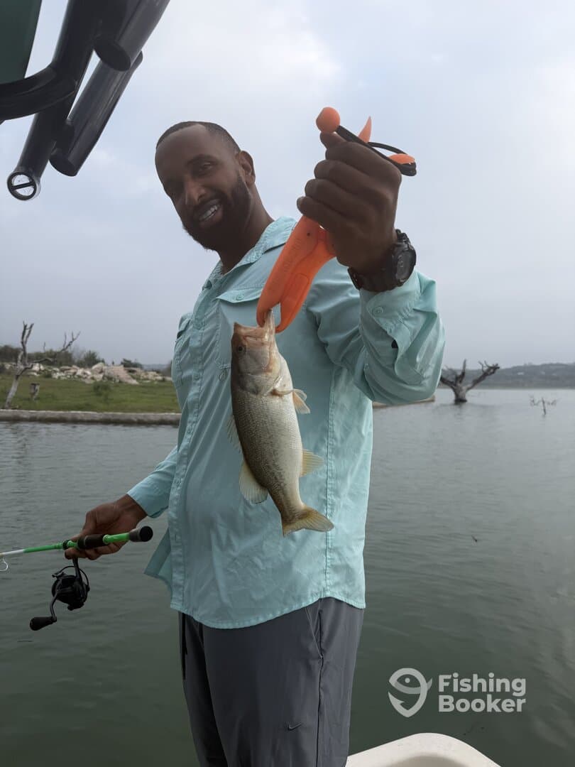 Angler proudly displaying a freshly caught Largemouth Bass while fishing from a boat in a serene lake setting.
