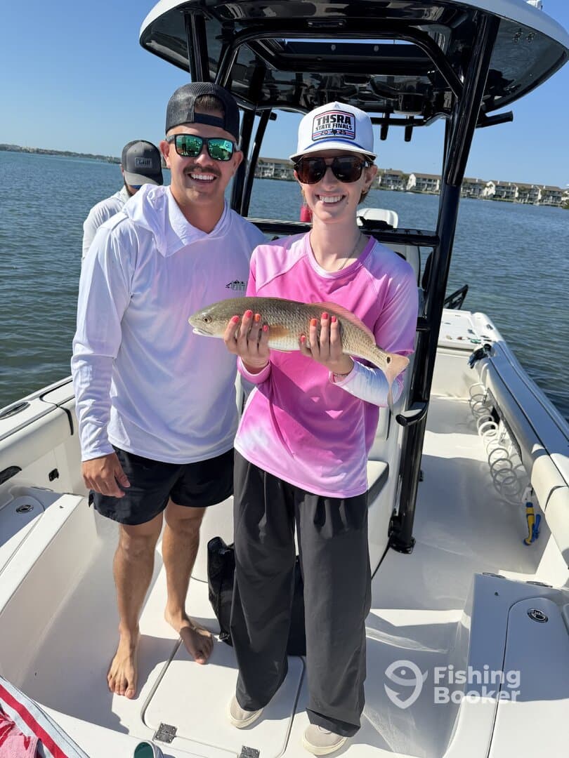Two anglers proudly displaying a Redfish on a sunny day aboard a fishing boat.