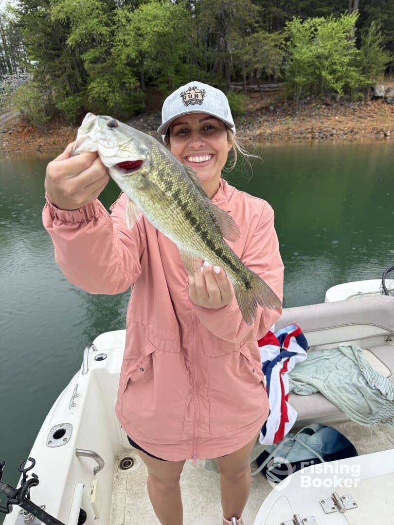 A happy angler proudly displaying a large Largemouth Bass while fishing on a serene lake.