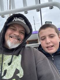 A smiling adult and a young boy pose for a selfie on a fishing boat, showcasing a bonding moment before their fishing adventure.