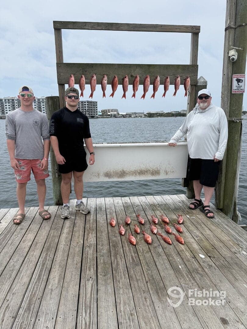 A group of three anglers proudly displaying their catch of Red Snapper on a catch board at the dock, showcasing a successful fishing trip.
