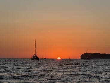 A serene sunset over the ocean with several boats silhouetted against the vibrant sky, creating a picturesque fishing environment.