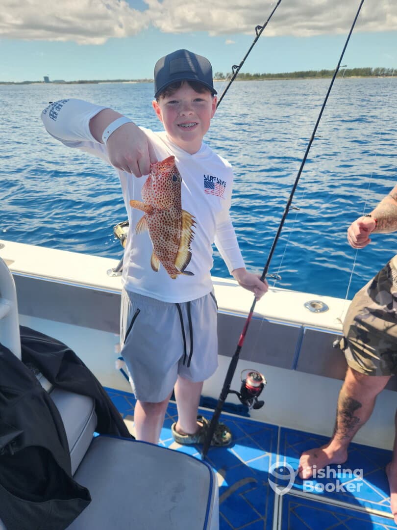 A young angler proudly displaying a colorful Snapper while fishing on a boat in clear blue waters.