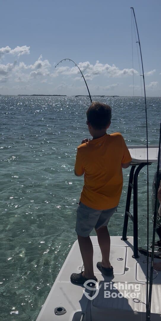 A young angler is actively reeling in a fish while fishing from a boat in clear waters, showcasing the excitement of the catch.