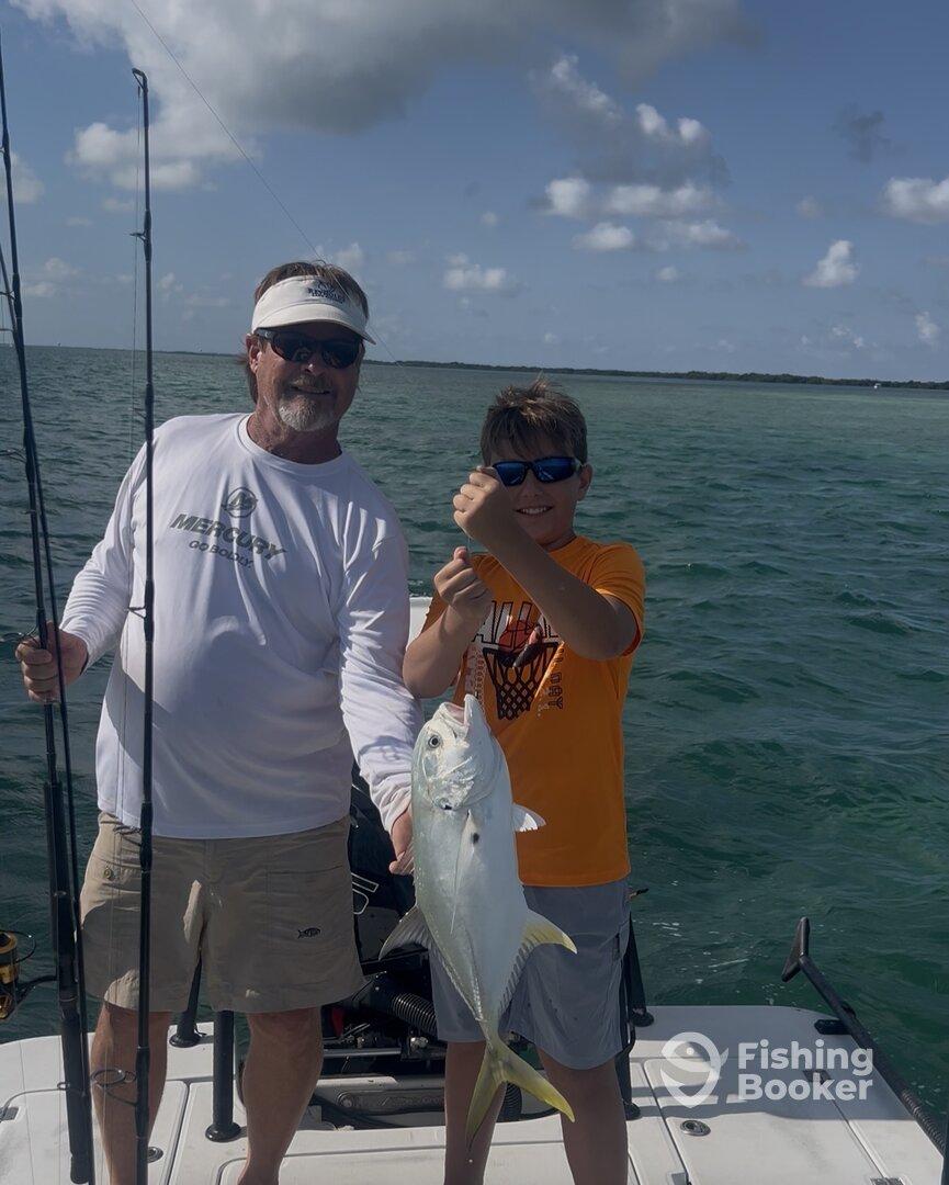 A young angler and an adult proudly displaying a caught fish while fishing on a boat in clear waters.
