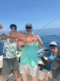 Group of anglers celebrating a successful catch of a large Red Grouper while out on the open water.