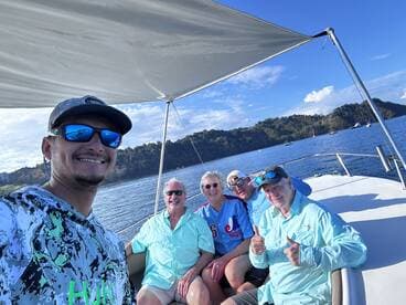A cheerful group of four anglers enjoying their time aboard a fishing boat, surrounded by scenic waters and hills.