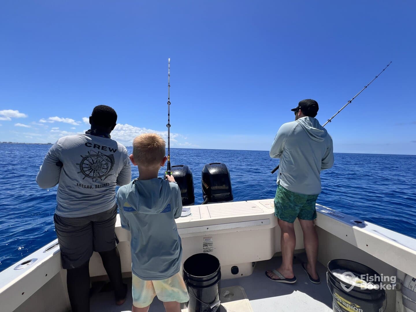 A young boy and crew member are actively fishing from a boat in the Bahamas, enjoying a sunny day on the water.