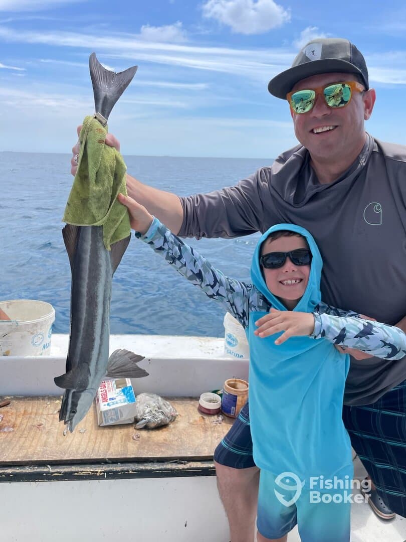A proud father and son duo showcasing a large fish on a fishing trip, with the ocean in the background.
