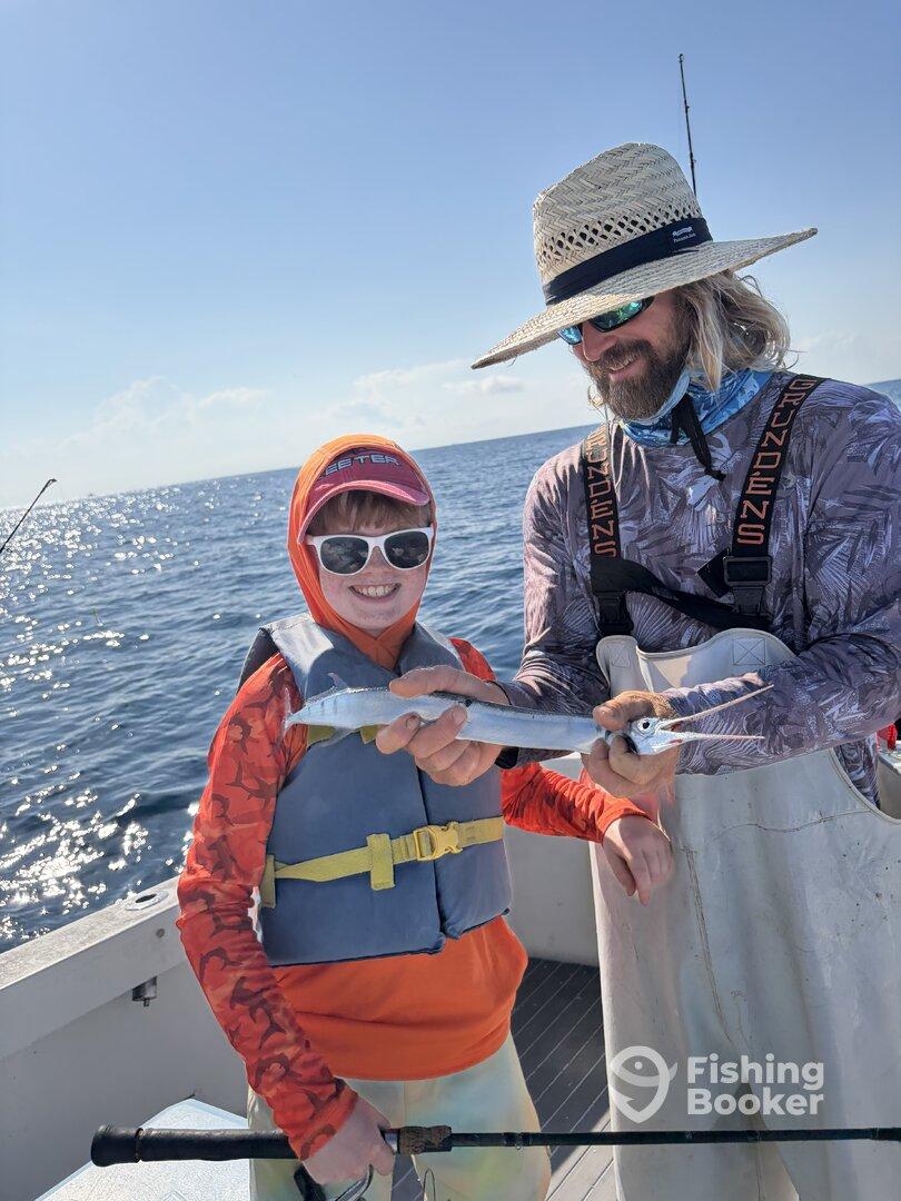 A young angler proudly holds a fish while fishing with an adult on a boat, showcasing a fun day on the water.