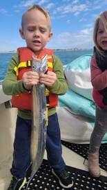 A young angler proudly displaying a fish while wearing a life jacket on a boat, with another child in the background.