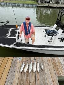An angler proudly displaying a catch of Speckled Trout on a dock after a fishing trip, with a boat visible in the background.