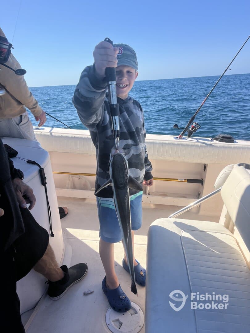 A young angler proudly displaying a caught fish aboard a fishing boat, enjoying a day on the water.
