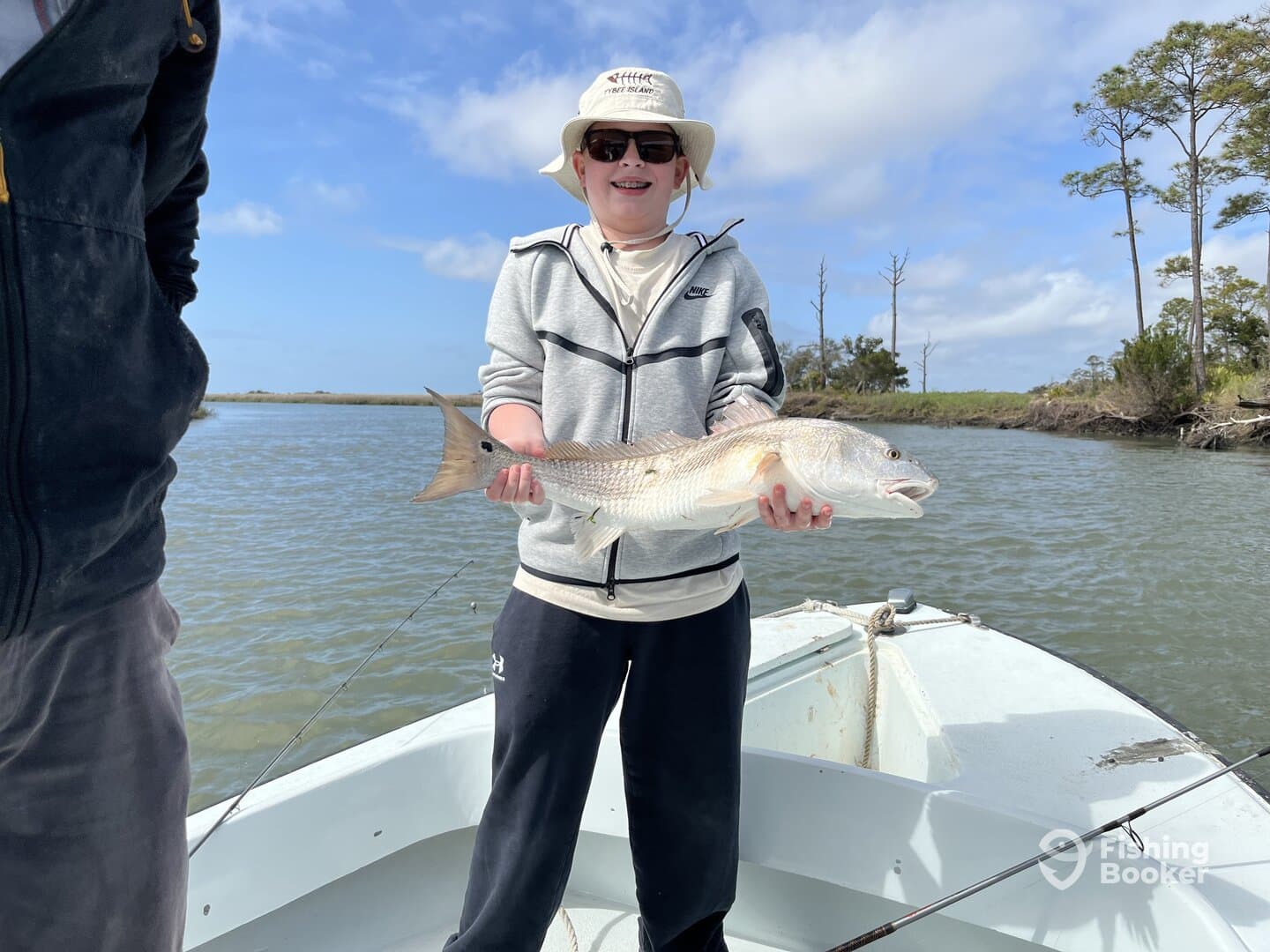 A young angler proudly displaying a Redfish while fishing from a small boat in a scenic coastal environment.