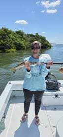 A smiling angler proudly displaying a Snook caught while fishing in a scenic mangrove area.