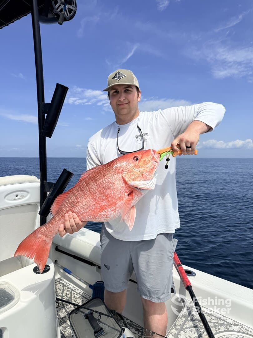 Angler proudly displaying a large Red Snapper while fishing on a boat in open waters.