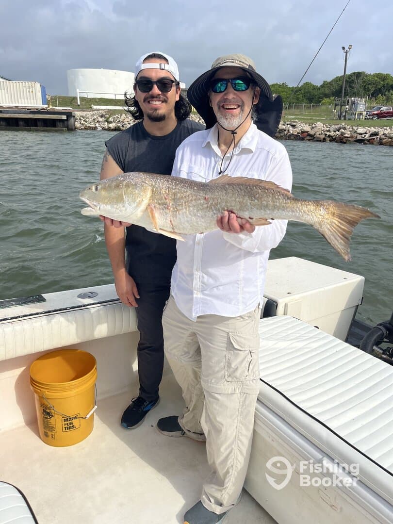 Two anglers proudly displaying a large Redfish while on a boat, showcasing a successful fishing trip.