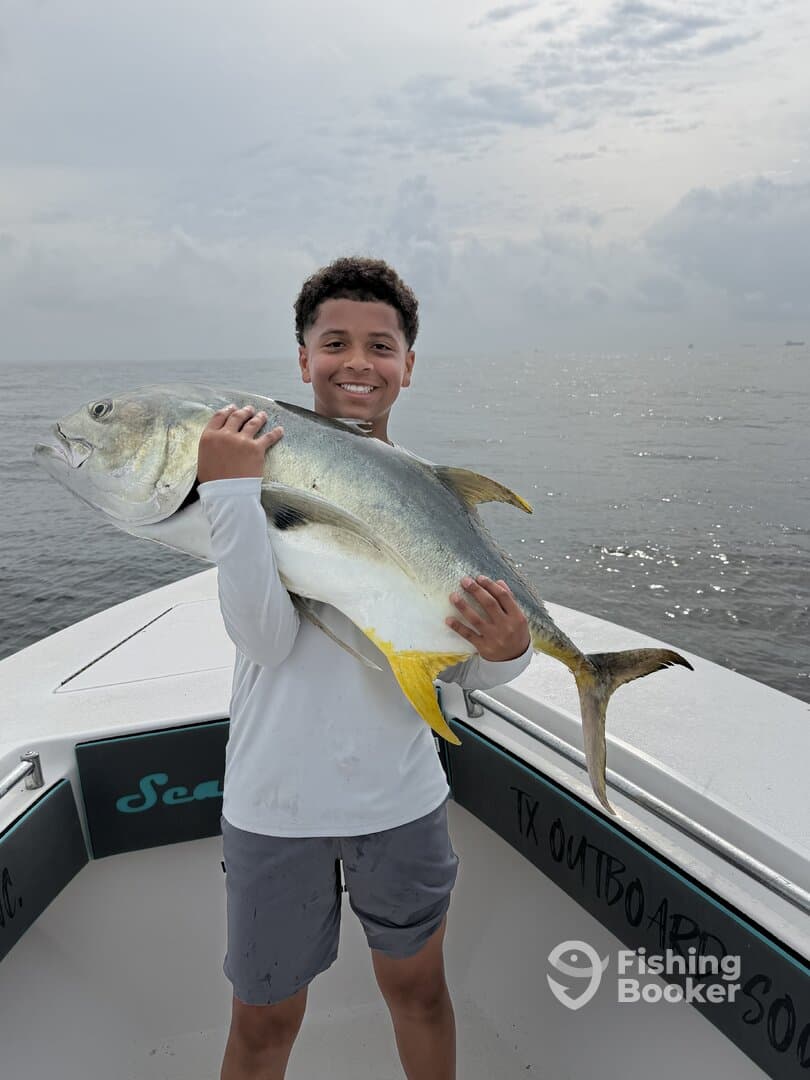 Young angler proudly holding a large Jack Crevalle aboard a fishing boat, showcasing a successful day on the water.