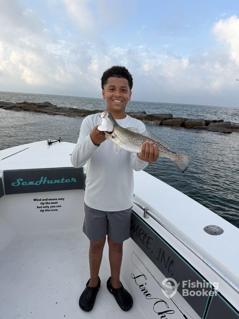 A young angler proudly displaying a Speckled Trout on the deck of a SeaHunter boat during a fishing trip.