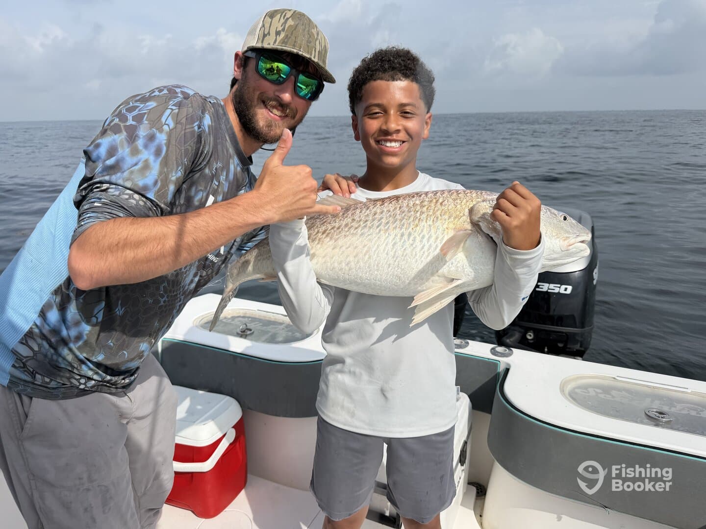 A young angler proudly displaying a large Redfish while fishing on a boat, showcasing a successful day on the water.