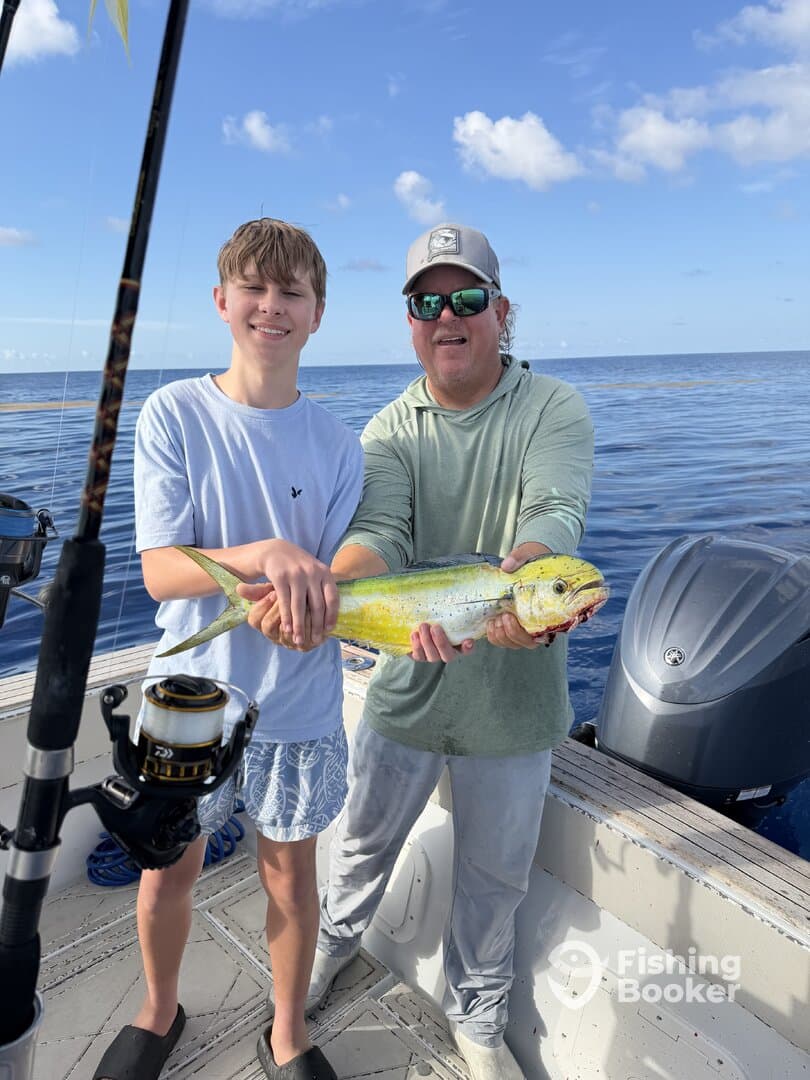 A young angler and an adult proudly displaying a vibrant Mahi Mahi while fishing on a sunny day.