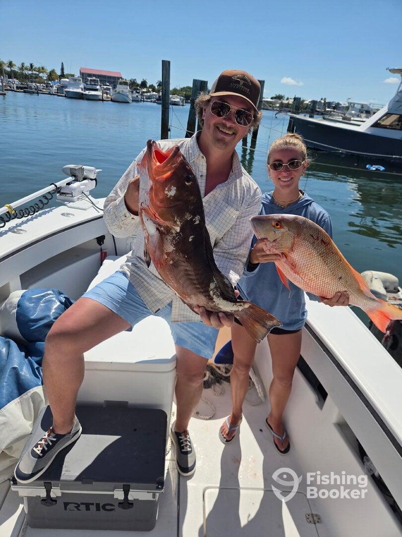Two anglers proudly displaying their catch of a large Grouper and Snapper aboard a fishing boat, showcasing a successful day on the water.