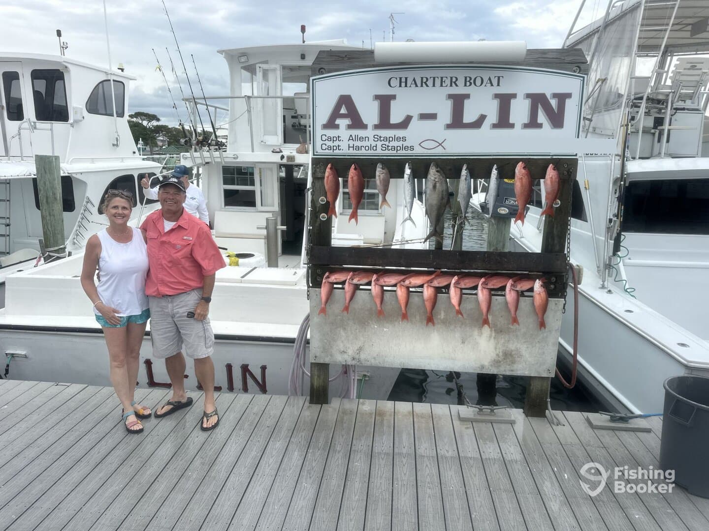 A couple poses in front of a catch board displaying a variety of fish, including Snapper, after a successful fishing trip on the charter boat Al-Lin.